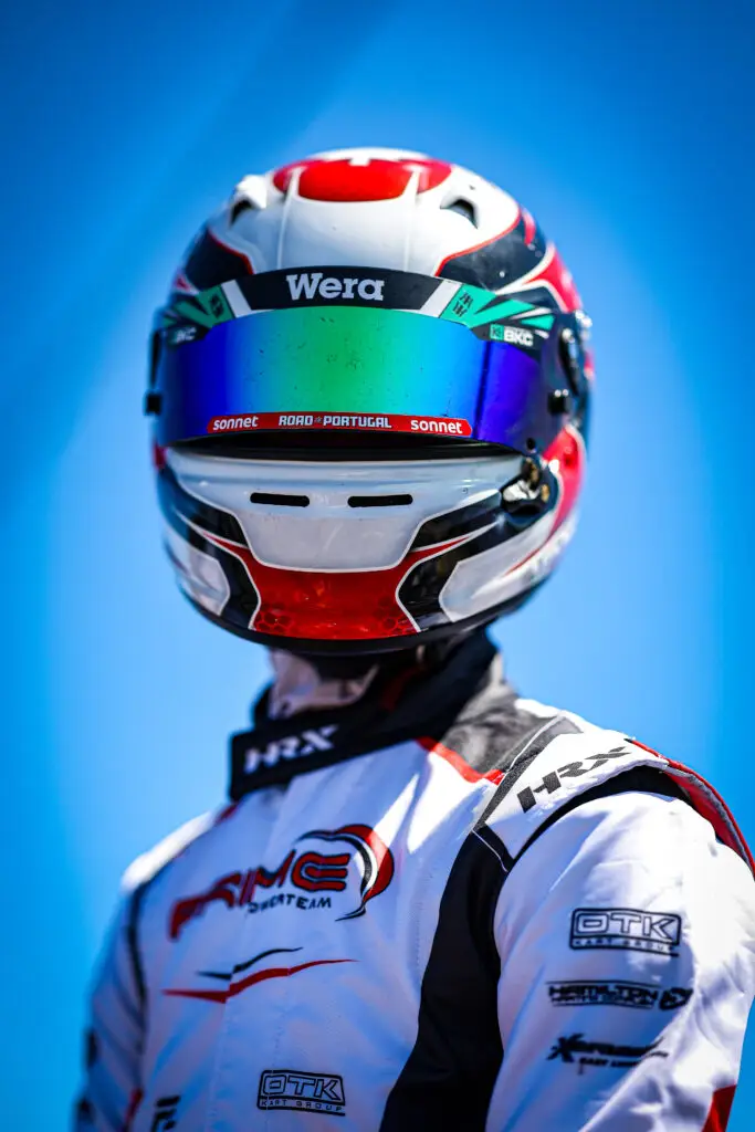 Close-up of a racing helmet on a rider, blue sky in the background, with a white-red helmet featuring 'Wera' and brand stickers